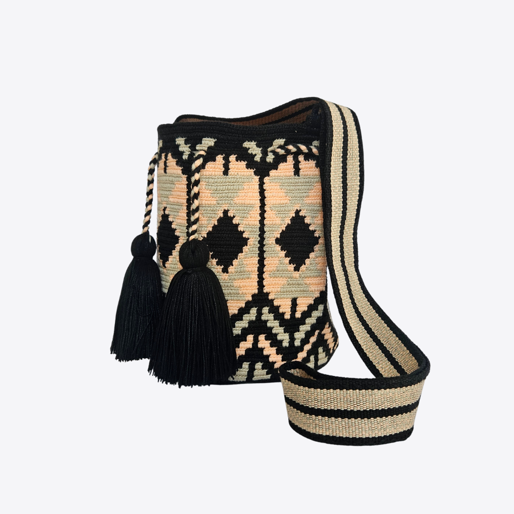 A handwoven bucket bag with a black and beige geometric pattern, featuring two black tassels and a wide woven shoulder strap, shown on a light gray background.
